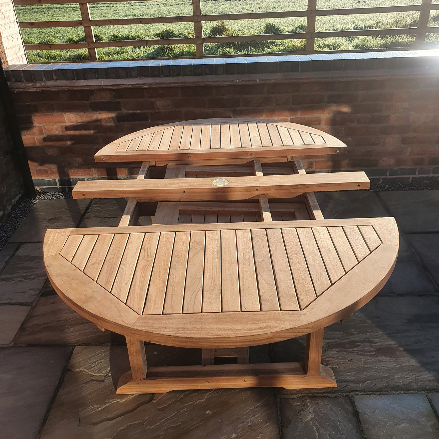 Two Round To Oval 120-170cm Extending (6 Seat Oxford Stacking Set) benches on a brick patio, arranged to form a circle around a small, central table, in bright sunlight.