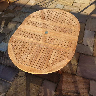 A Teak Garden Furniture Round To Oval 120-170cm Extending Table, featuring slatted top design, sitting on a tiled patio floor in sunlight.