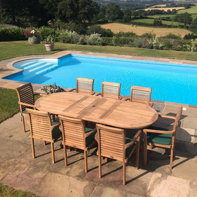 Outdoor dining set with eight Oxford Stacking chairs around a Premium Teak Oval 180-240cm table by a rectangular pool, overlooking a lush landscape on a sunny day.