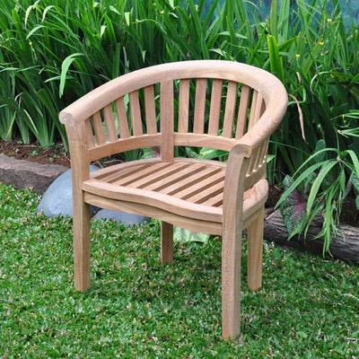 A Teak 120cm Sunshine Set with 4 San Francisco Chairs with a curved backrest and slatted seat, placed on grass surrounded by lush green plants.