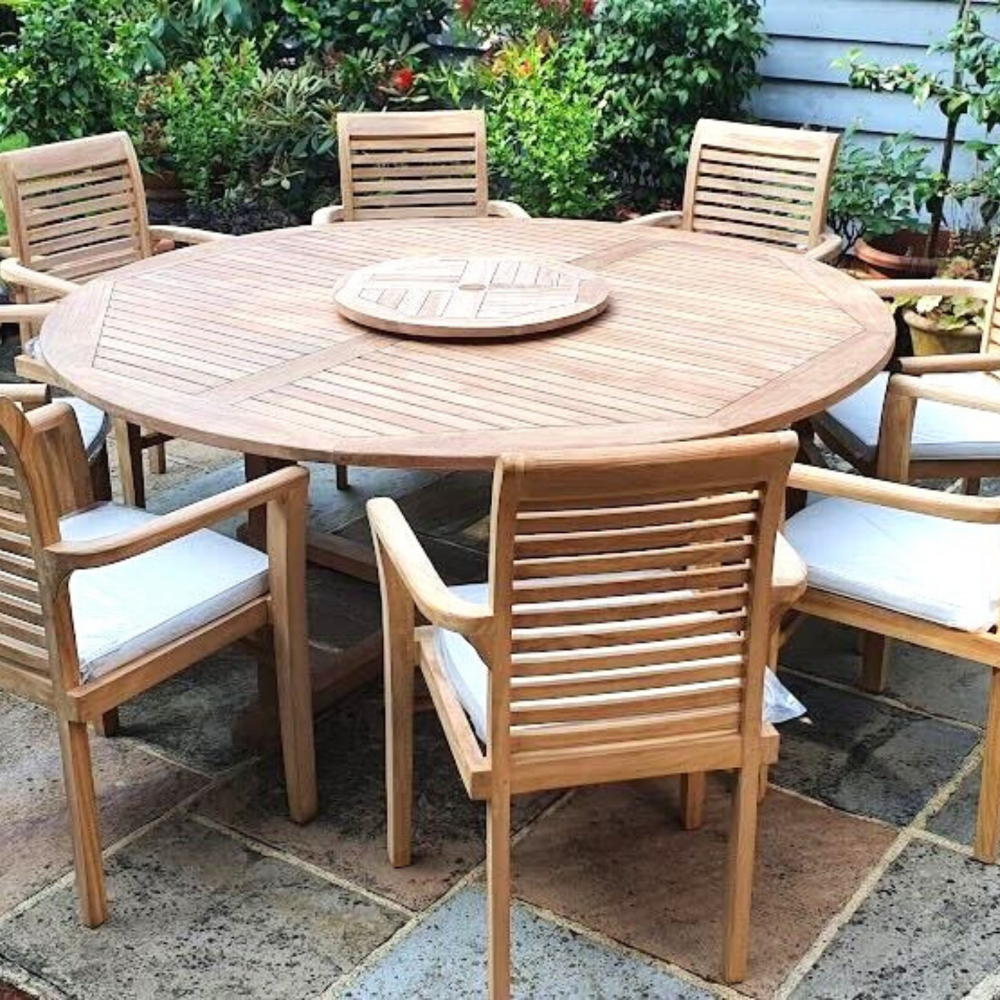 Teak 180cm Maximus Round Stacking Set (8 Oxford Stacking Chairs) Complete set Cushions included comprising a round table and six chairs with white cushions, surrounded by potted plants.