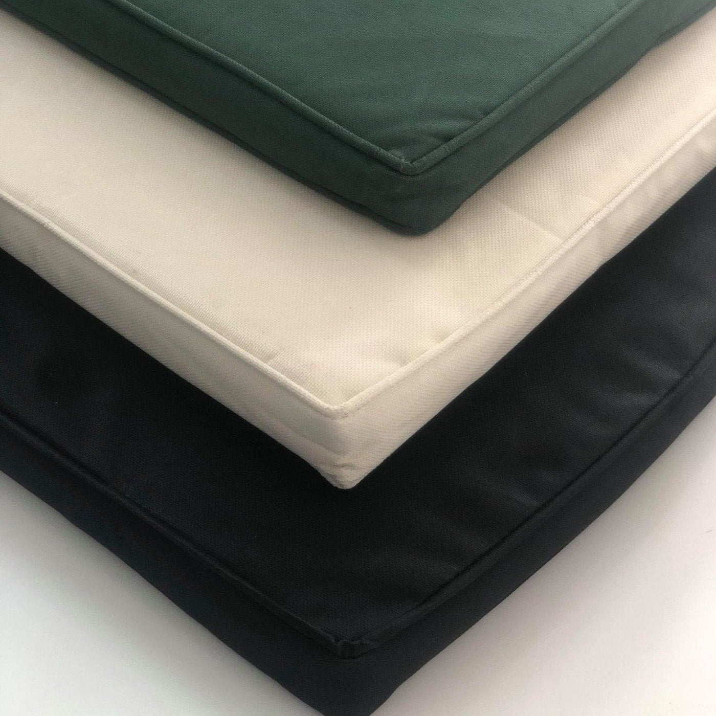 A stack of square cushions in black, white, beige, and green, arranged neatly on a Teak 180cm Maximus Round Stacking Set (8 Oxford Stacking Chairs) Complete set Cushions included.