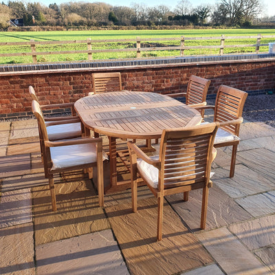 A Round To Oval 120-170cm Extending (6 Seat Oxford Stacking Set) with six chairs on a paved patio, overlooking a rural landscape with a fenced pasture under a clear sky.