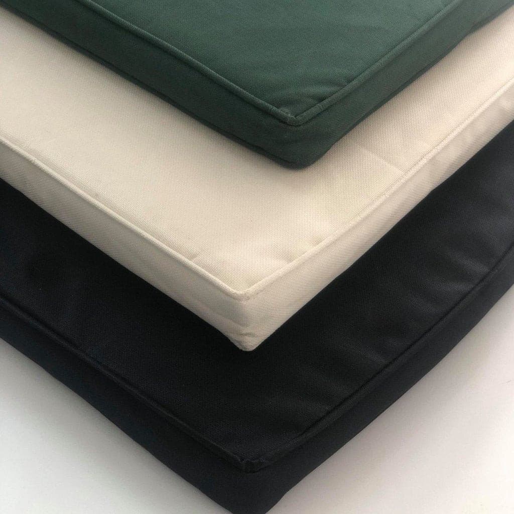 A stack of four square cushions in black, cream, forest green, and navy blue colors on a Teak 180cm Round Maximus Set (4 San Francisco Benches) Complete set Cushions Included.