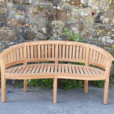 Teak 180cm Round Maximus Set (3 San Francisco Benches) Complete set Cushions Included curved bench in front of a weathered stone wall with small plants growing at its base.