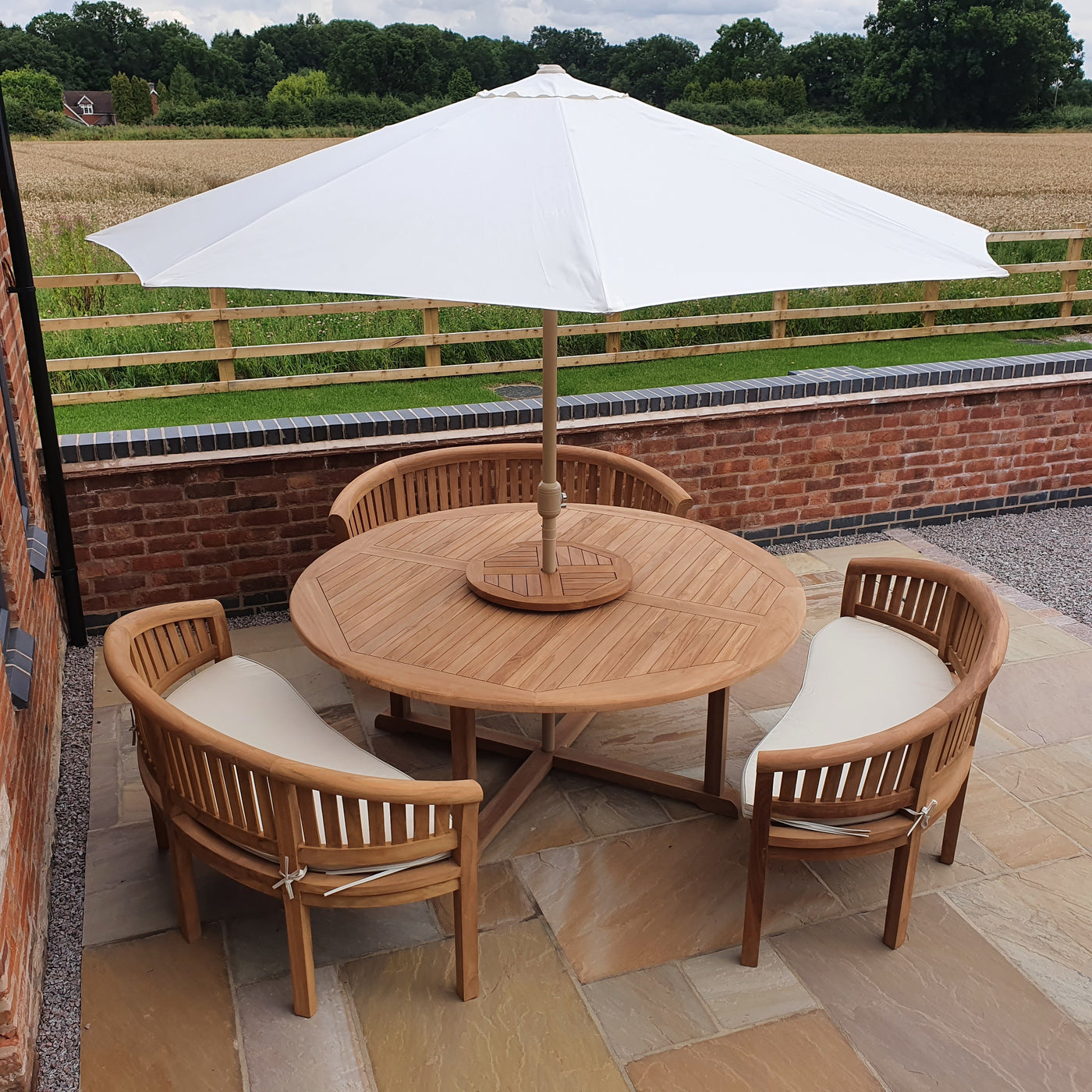 Outdoor patio setup with a Teak 180cm Round Maximus Set (3 San Francisco Benches) complete set cushions included, overlooking a field.