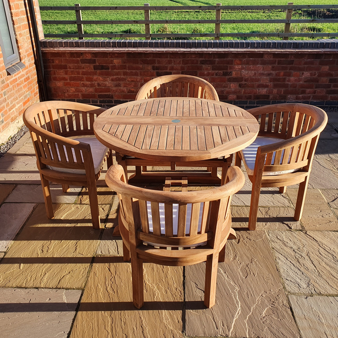 A Round To Oval 120-170cm Extending Table & 4 San Francisco Chairs Complete set Cushions Free Delivery and four matching chairs on a brick patio, with green grass and a brick wall in the background.