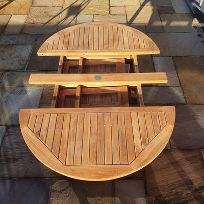 Top view of a Round To Oval 120-170cm Extending Table & 4 San Francisco Chairs Complete set Cushions Free Delivery featuring a wooden round table with two semi-circular benches on a paved surface, lit by sunlight.