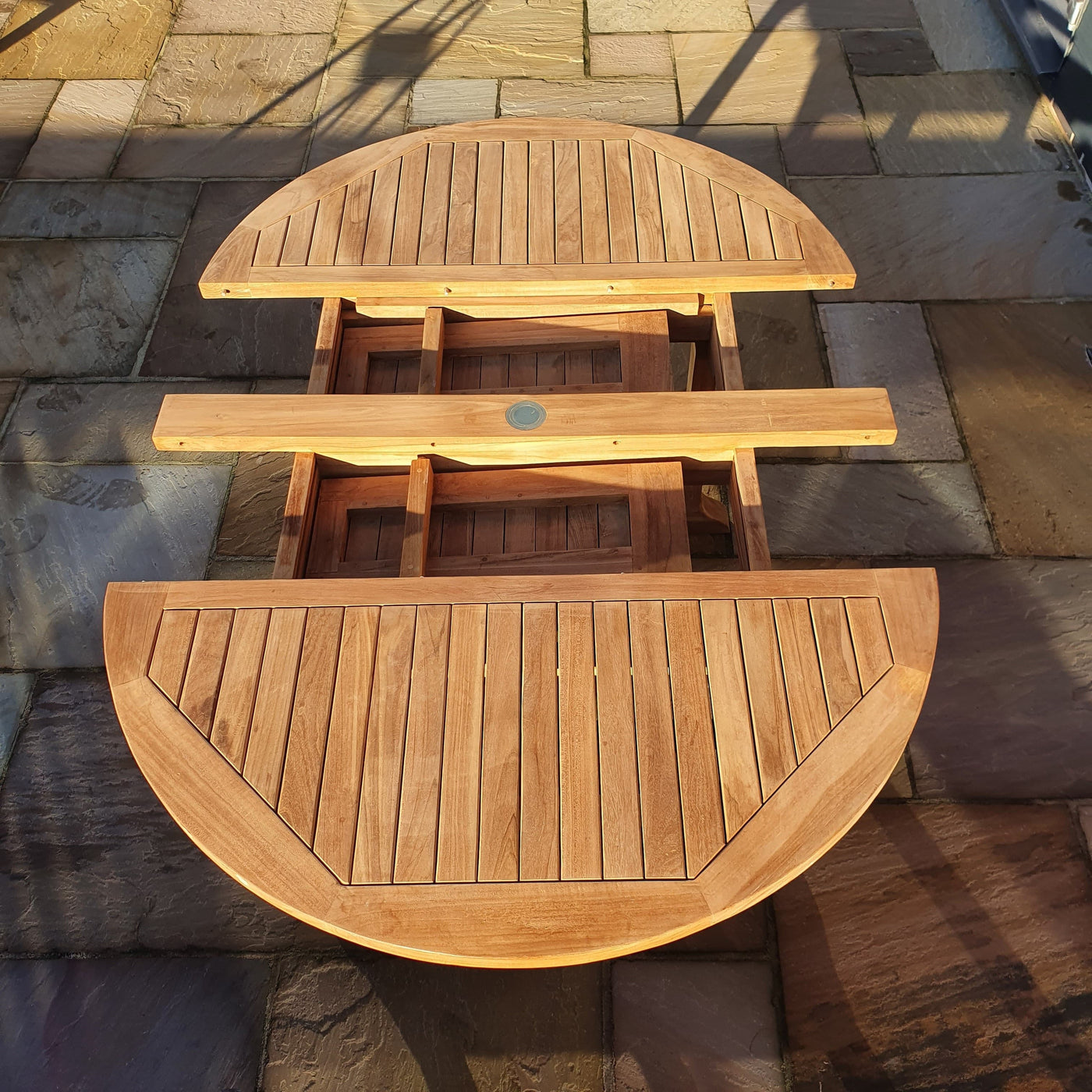 Oval 120-170cm Extending 2 Seat Stacking & 4 Folding Chair Complete set Cushions Free Delivery round table folded down on a stone patio under sunlight.