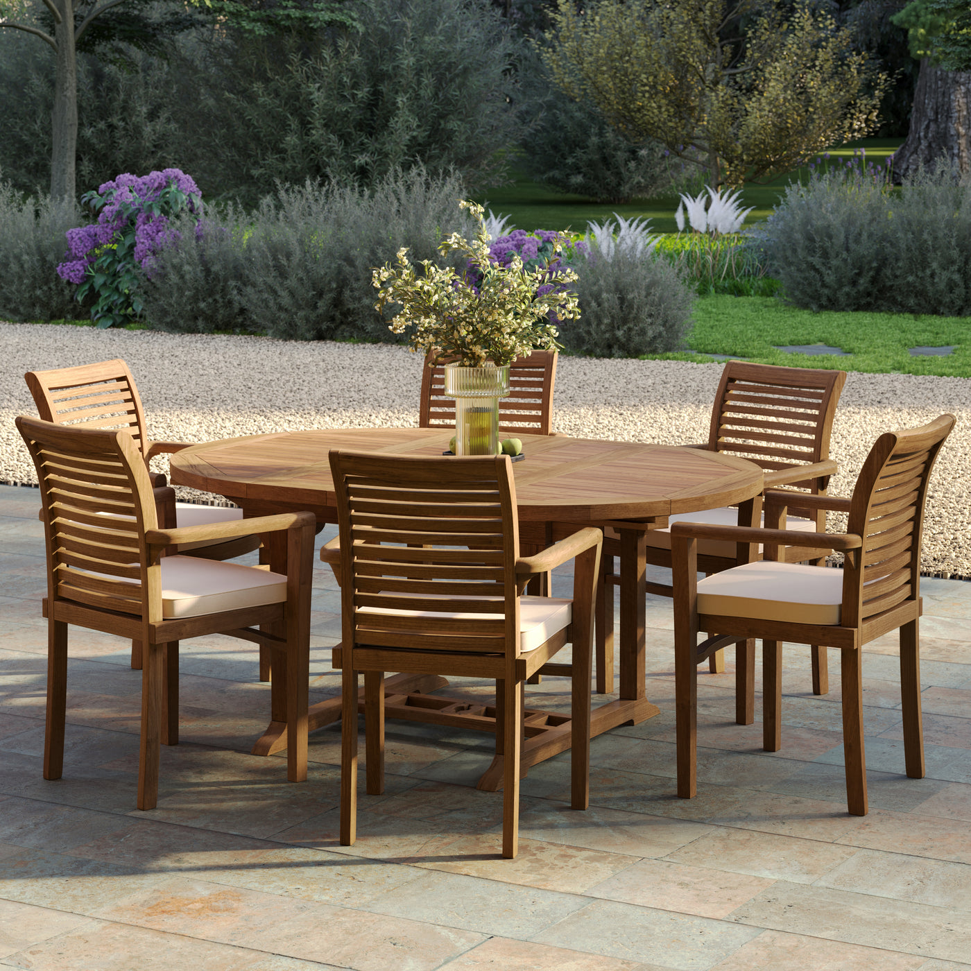 Round to oval teak dining table and six stacking chairs, part of a premium teak garden furniture set placed on a stone patio near flower beds.