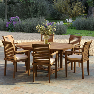 Round to oval teak dining table and six stacking chairs, part of a premium teak garden furniture set placed on a stone patio near flower beds.