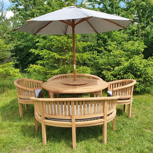 A Teak Garden Furniture set including a 150cm round teak table, 2 San Francisco benches, and 2 San Francisco chairs under an open white umbrella, set against a backdrop of lush greenery.