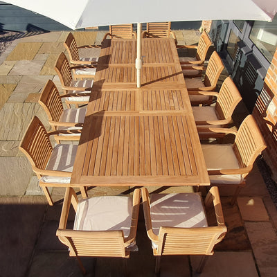 Outdoor dining area with Giant 2-3m Teak Extending Rectangle Table (12 Oxford Stacking Chairs) Complete set Cushions included under a white umbrella on a brick patio.